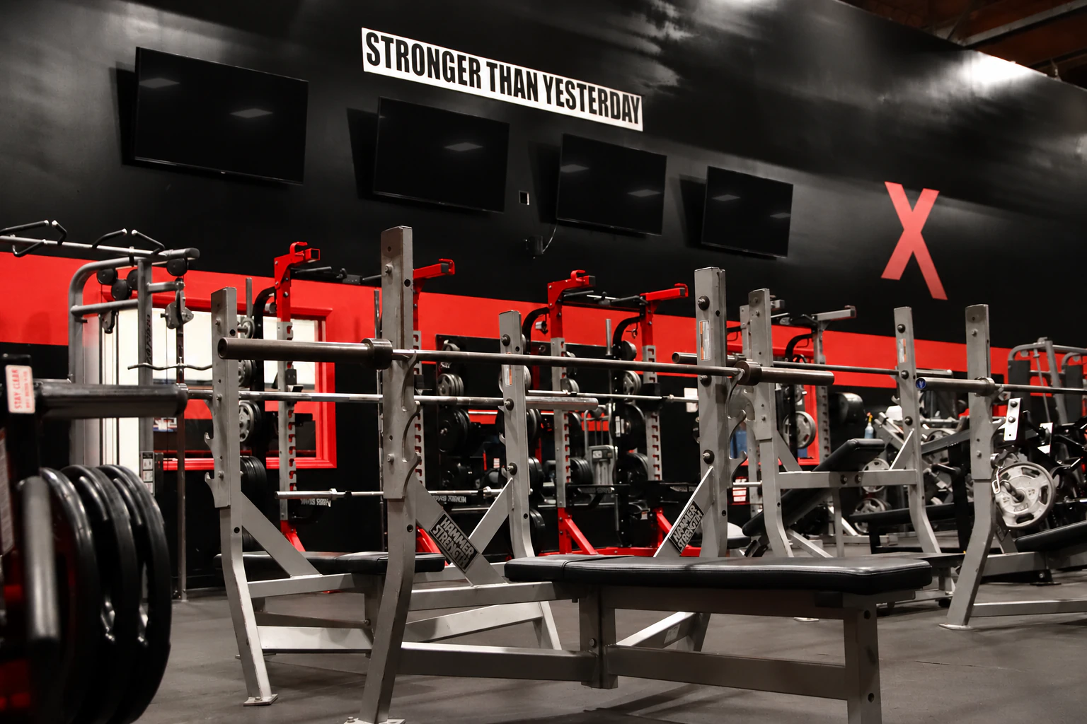 Barbell bench press and squat stations under the Stronger Than Yesterday wall at XCEL in Fairfield, NJ
