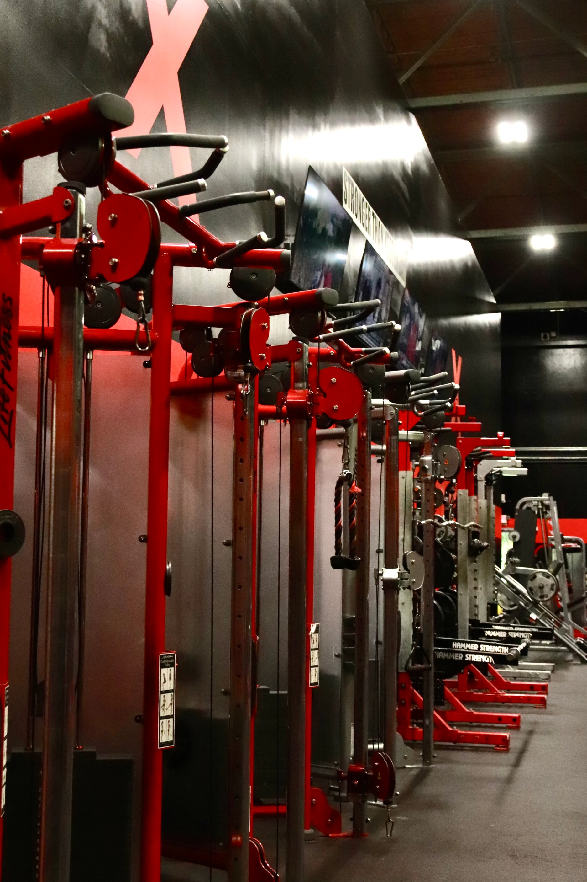 Row of red Hammer Strength cable stations on the strength floor at XCEL Sports & Fitness in Fairfield, NJ