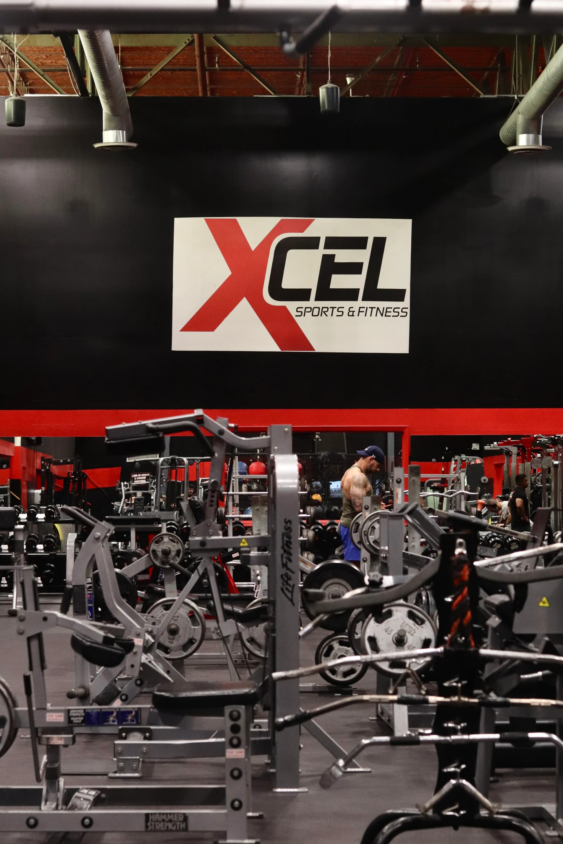 Member training on the strength floor under the XCEL sign at XCEL Sports & Fitness in Fairfield, NJ