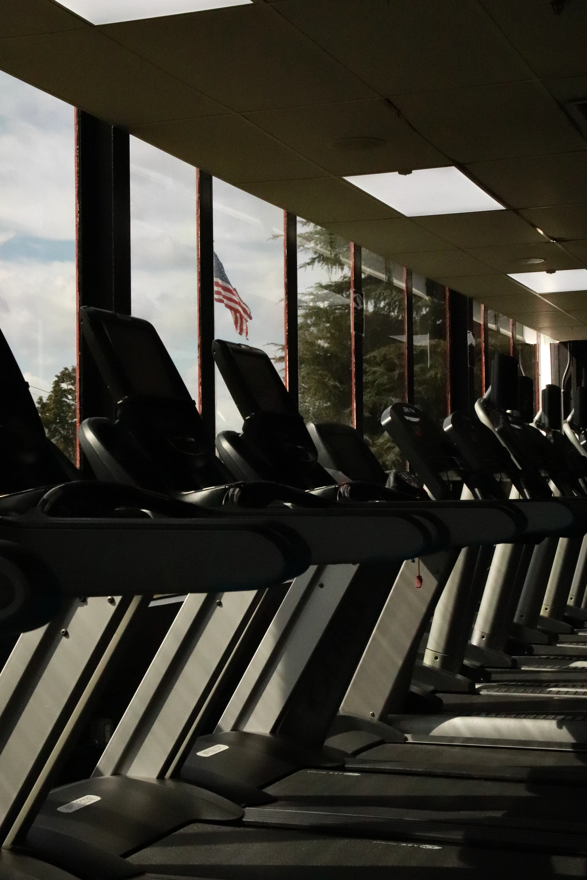 Treadmills along the windows with an American flag outside at XCEL Sports & Fitness in Fairfield, NJ