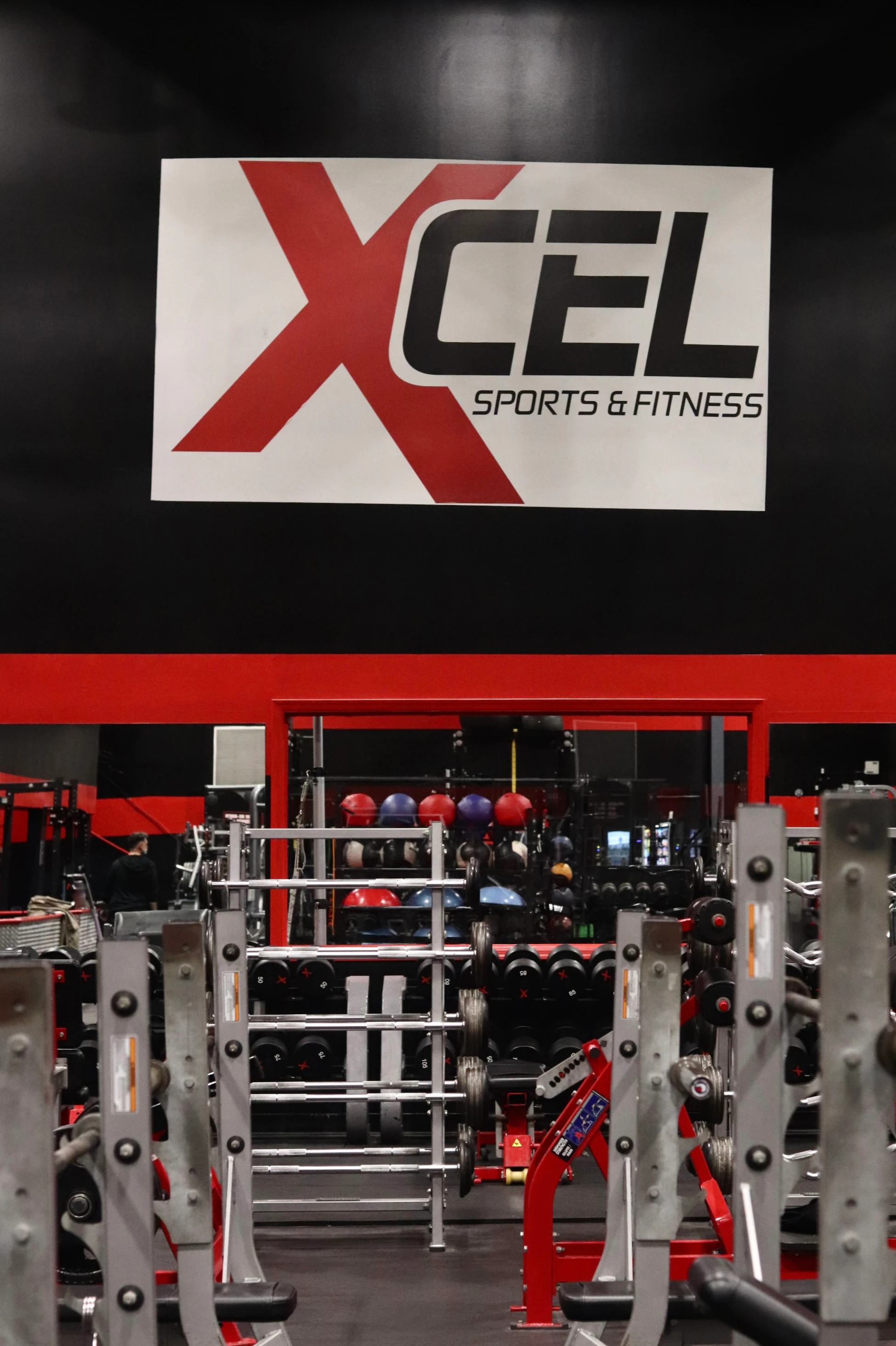 XCEL Sports & Fitness sign above squat racks and medicine balls at the gym in Fairfield, NJ